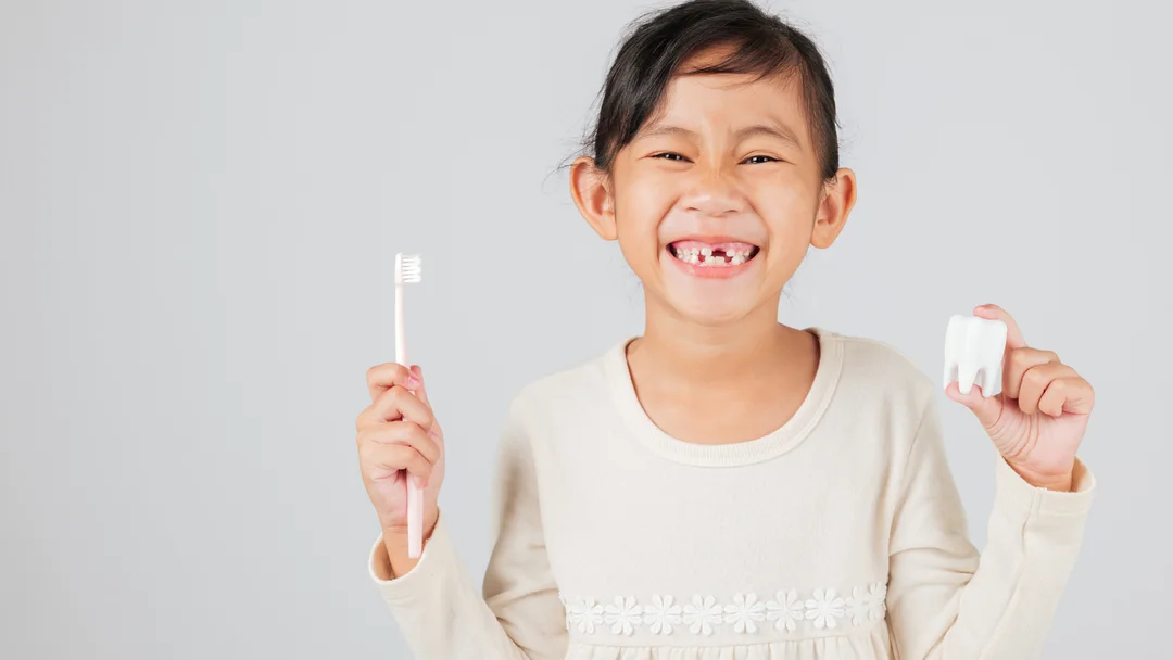 A young patient smiling at Akron Family Dental, holding a toothbrush and a model tooth